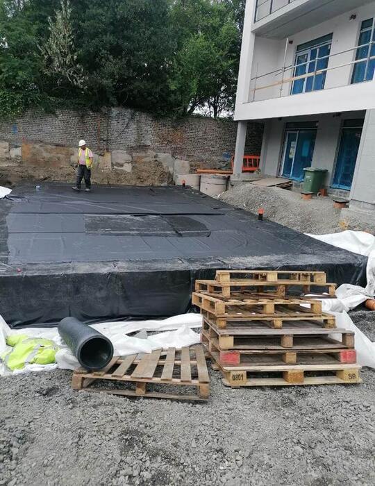 Construction site with worker, wooden pallets, black pipe and blue building